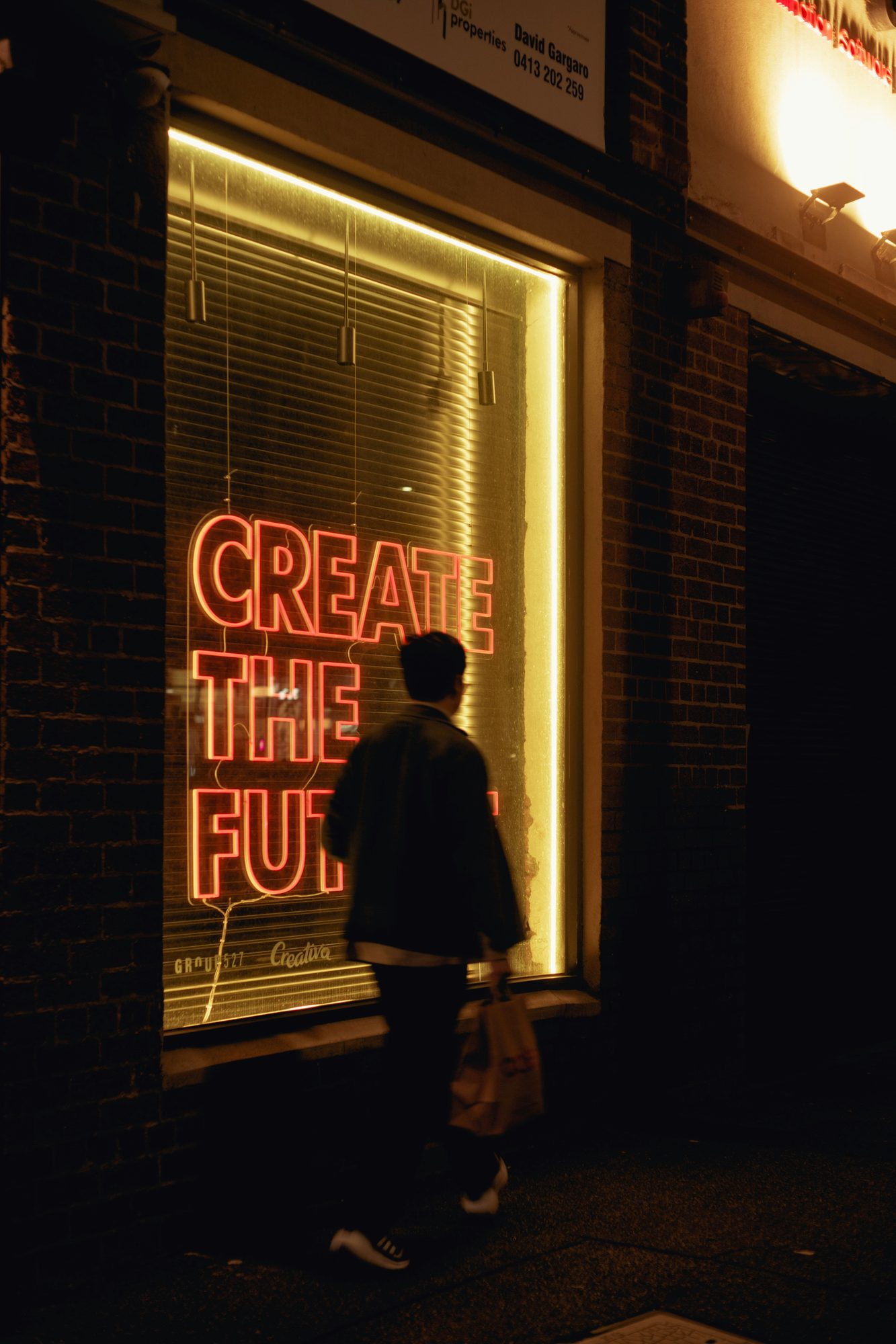 Neon sign reading Create the Future in a city window at night
